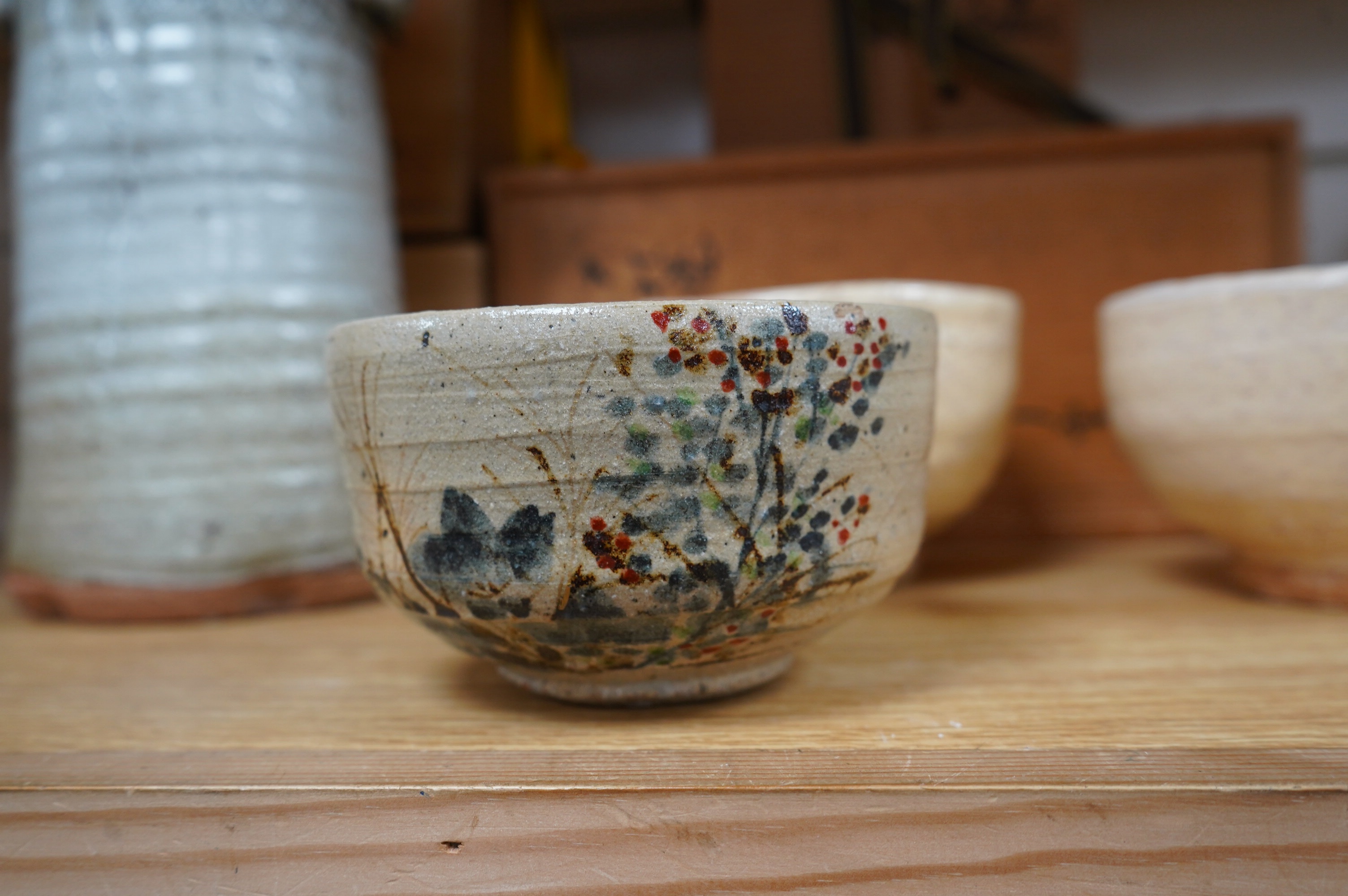 Japanese studio pottery comprising a Nishiyama (Contemporary Japanese School) tea bowl in the Yashichida style decorated with flowers (fitted box), a near pair of Japanese studio pottery cream ground raku bowls (fitted b